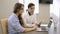 Young colleagues talking while sitting at table with laptop and tablet in company.