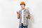 Young concerned handsome man in protective orange hardhat holding toy screwdriver and adjustable wrench isolated on
