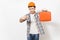 Young concerned man in protective hardhat pointing index finger on case with instruments or toolbox isolated on white