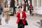 Young confident businesswoman in formalwear, red jacket is talking on smartphone while walking on city street