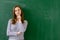 Young confident smiling female high school student standing in front of chalkboard in classroom.