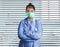 Young confident and successful Asian Chinese medicine doctor woman in hospital scrubs and mask posing at venetian blinds