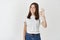 Young confident woman standing on white background and showing okay sign, confirm and approve something, praise good