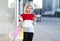 young consumer woman standing by a fashion store window display holding paper shopping bags and using a smartphone