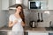 Young contented woman holding white mug in kitchen wearing a white t-shirt