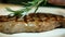 Young cook puts rosemary branches on fried meat in kitchen of restaurant.