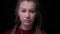 Young cool brunette girl with piercing and dreadlocks watches modestly and calmly into camera on black background.