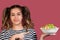 Young cool girl pointing to the bowl with fresh salad looking at camera