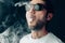 Young cool guy in sunglasses exhales a cloud of smoke. Studio horizontal portrait in close-up.