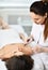 Young cosmetician prepares the patient`s face for a cosmetic procedure by applying a special composition with a brush