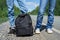 A young couple, below the waist, standing with a backpack at their feet on the side of the road. The concept of