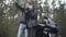 Young couple of bikers standing in spring or autumn forest and looking away using binoculars. Confident Caucasian woman