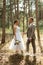 young couple bride in a white short dress and groom in a gray suit in a pine forest