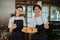 young couple of cake makers wearing aprons with thumbs up as a plate of baked cookies