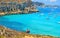 Young couple are coming down towards Turquoise lagoon paradise beach Cala Rossa with people swiming on Favignana island in Sicily,