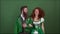 Young couple in costumes celebrating saint patrick`s day isolated on green wall dancing together