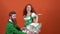 Young couple in costumes celebrating Saint Patrick`s Day isolated on orange wall traditional dance