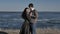 Young couple dressed in dark walks along the seashore, sunny day