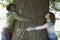 Young Couple Embracing Tree Trunk At Park