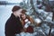 Young couple embracing among trees covered snow. Leisure activity in park. Coffee cups in hands.