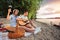 Young couple enjoying their time, having romantic picnic at the beach. Playing guitar and singing