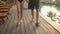 Young couple feet walk barefoot along swimming pool at tropical hotel. Boyfriend and girlfriend fit legs go at wooden