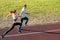 Young couple of fit sportsmen boy and girl running while doing exercise on red tracks of public stadium outdoors