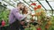 Young couple florists work in garden center. Attractive man and woman in apron count flowers using tablet computer