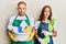 Young couple of girlfriend and boyfriend wearing apron holding products and cleaning spray clueless and confused expression