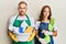 Young couple of girlfriend and boyfriend wearing apron holding products and cleaning spray relaxed with serious expression on face