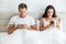 Young couple handsome husband and his beautiful wife just woke up in bed checking their smartphones early in the morning