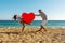 Young couple having fun on the beach with a big heart balloon. Summer love concept