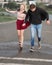 Young couple holding hands run on street with splashing in puddles