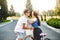 Young couple hugging on road on sunset. Pretty girl with long curly hair in hat and long skirt holds a bike, handsome