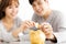 young Couple Inserting Coin In Piggybank