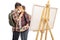 Young couple kissing next to a canvas and hiding their faces with paintbrushes