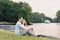 A young couple in love, a guy and a girl are sitting on the shore of the lake, happy and smiling. First date