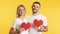 Young couple in love holding big paper hearts in hands over studio background