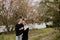 Young Couple in Love Holding One Another Outside in Nature in From of Cherry Blossom Tree and Pond