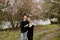 Young Couple in Love Holding One Another Outside in Nature in From of Cherry Blossom Tree and Pond