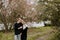 Young Couple in Love Holding One Another Outside in Nature in From of Cherry Blossom Tree and Pond