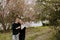 Young Couple in Love Holding One Another Outside in Nature in From of Cherry Blossom Tree and Pond