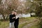 Young Couple in Love Holding One Another Outside in Nature in From of Cherry Blossom Tree and Pond