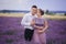 Young couple in love hugging and walking in a lavender field on summer cloudy day. girl in a luxurious purple dress and with