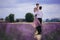 Young couple in love hugging and walking in a lavender field on summer cloudy day. girl in a luxurious purple dress and with