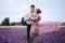Young couple in love hugging and walking in a lavender field on summer day. girl in a luxurious purple dress and with hairstyle