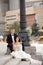 Young couple in love, lamppost, wedding suits and dress on background of old city sitting on stairs, happy wedding day together.