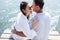 Young couple in love in light casual clothes is sitting on wooden bridge. Happy woman and man hug and laugh on background of sea