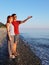 Young couple in love stand on pebble beach in the evening light and man shows with his hand to copy space