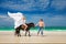 Young couple in love walking with the horse on a tropical beach.